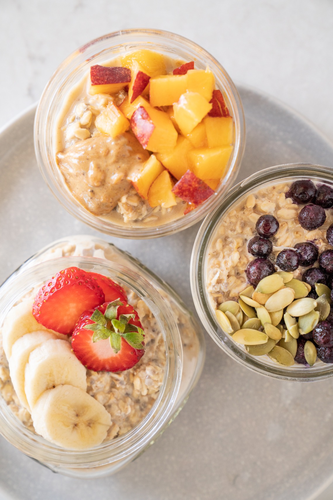 Overnight Oats in seperate jars with each different toppings: strawberries & bananas, Chocolate chips & nuts, Peaches & honey
