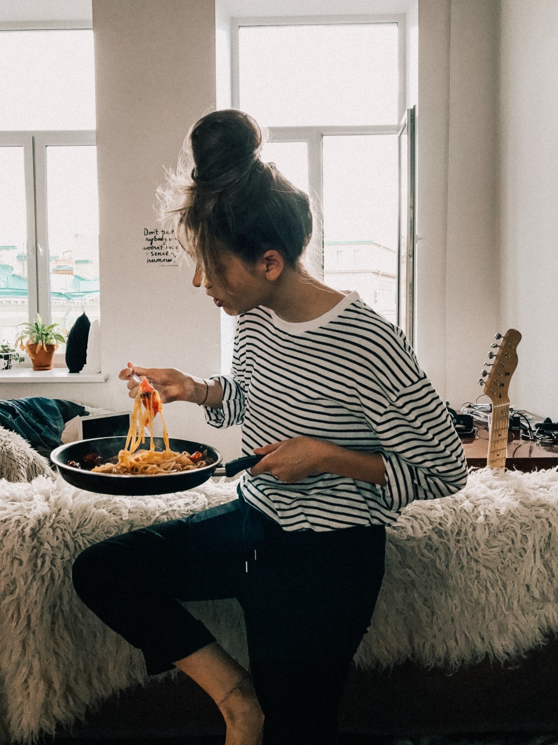 women in striped shirt eating pasta in apartment